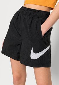 Pantaloni corti neri realizzati in tessuto leggero e testurizzato, con vita elastica e tasche laterali. Grande grafica del marchio Nike di colore bianco sul lato.