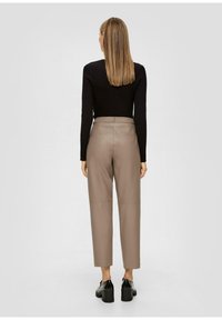 Bruine faux leren hoge taille broek met een rechte pijp, voorzien van achterzakken, gecombineerd met een zwart geribbelde top met lange mouwen en zwarte schoenen.
