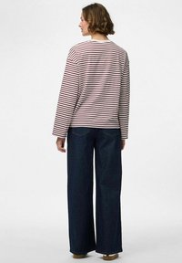 Gestreepte lange mouwen shirt in crème en bordeaux, gecombineerd met wijde donkere denim jeans. Heeft een ronde hals en een relaxte pasvorm.