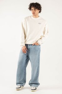 Sweatshirt beige chiaro con maniche lunghe e collo rotondo, abbinato a jeans blu chiaro a vestibilità ampia e sneaker bianche con accenti blu.
