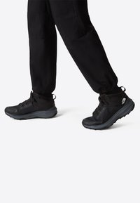 Svarta vandringssandaler med övre i mesh och syntetmaterial, vadderad krage och texturerad gummisula, i kombination med svarta avsmalnande byxor.