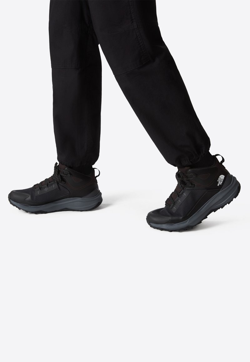 Svarta vandringssandaler med övre i mesh och syntetmaterial, vadderad krage och texturerad gummisula, i kombination med svarta avsmalnande byxor.