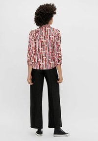 Chemise à boutons avec un motif géométrique vif en rouge, rose et noir, avec des manches trois-quarts, associée à un pantalon large noir et des baskets.