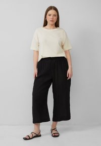 Crème korte mouwen T-shirt in combinatie met zwarte wijde broek met een trekkoord in de taille en zwarte platte sandalen met dunne banden.