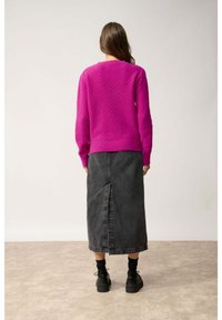 Pull en fuchsia texturé avec un ourlet côtelé, associé à une longue jupe en jean noir avec une fente centrale, le tout complété par des chaussures noires.