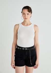 Top cu bretele albă cu striații, asortat cu pantaloni scurți negri din denim cu talie înaltă. Curea metalică cu linkuri decorative și detalii cu lanț.