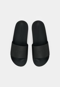 Pair of black Tommy Hilfiger slide sandals with textured straps and embossed brand name, displayed side by side on a white background.