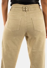 Beige corduroy broek met een ribbeltextuur, voorzien van achterzakken, een hoge taille en drukknoopdetails op de tailleband.