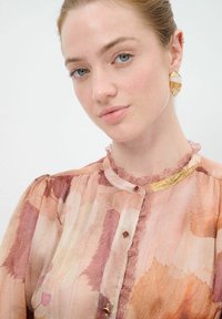 Voile-Bluse mit floralem rosa und beigen Muster, mit Rüschensaum, goldenen Akzenten und kleinen Knöpfen. Texturiert und leicht.