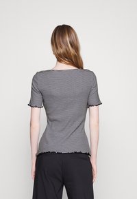 Black and white striped short-sleeve top with a rounded neckline and ruffled edges at sleeves and hem. Fitted design, soft fabric.