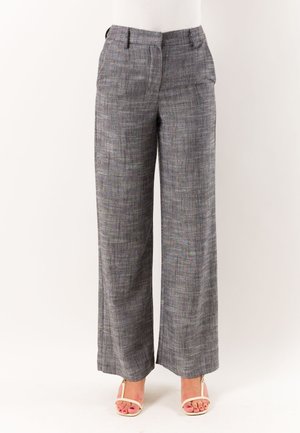 Pantaloni grigi a gamba larga su misura indossati con tacchi bianchi open-toe su uno sfondo bianco semplice.