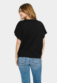 Sort kortærmet top med en afslappet pasform, har drop-skuldrer og en rund halsudskæring. Parret med lyseblå denimjeans.