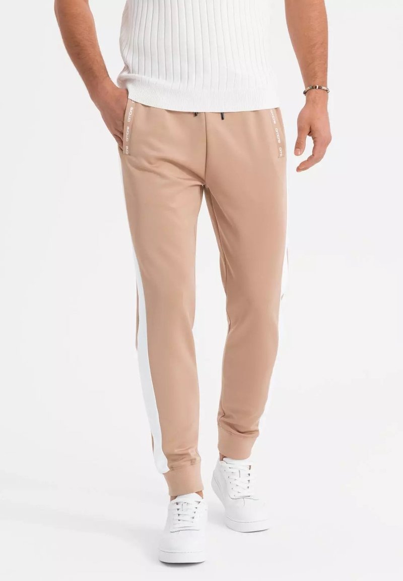 Beige joggerbroeken met witte zijstrepen, elastische tailleband en koord. Gecombineerd met witte sneakers en een gebreid, textuur top.