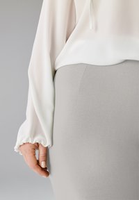 Leichte, halbtransparente weiße Bluse mit lockerem Schnitt und elastischen Ärmelbündchen, kombiniert mit einem figurbetonten grauen Rock mit glatter Textur.