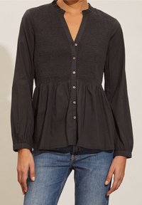 Svart knäppskjorta med smockad byst, långa ärmar, vågig krage och gathered nederdel. Sparsamma knappar och slät tygkvalitet.