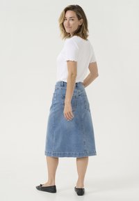 Blå denim A-linje kjol med bakfickor, knälång, tillsammans med en vit ribbad kortärmad topp med vågiga kanter.