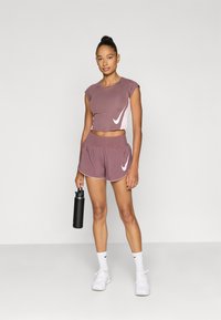 Αθλητική στολή σε μοβ απόχρωση με κοντό τοπ και ταιριαστά σορτς. Άσπλο λογότυπο Nike, απαλή υφή υφάσματος και ελαστική μέση στα σορτς.
