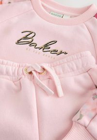 Ensemble de sweat-shirt rose et de joggers avec broderie dorée "Baker", taille élastique avec cordon de serrage, et accents à motif floral. Tissu doux.