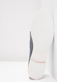 Scarpa grigia scura con tomaia liscia, texture perforata e suola in gomma bianca. Numero "37" segnato sulla suola.