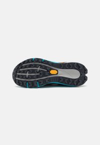 Semelle d'une chaussure de randonnée noire et grise avec des crampons profonds, des accents turquoise et le logo Vibram jaune au centre.