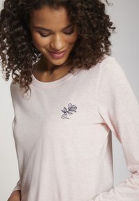 Helles rosa Langarmshirt mit navyblauer bestickter Blumengestaltung und Text in der Nähe des Halsausschnitts, gefertigt aus weichem, strukturiertem Stoff.
