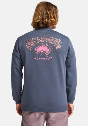 Blue sweatshirt with a graphic print on the back featuring the text "BILLABONG" and an outline of Australia in pink. Long sleeves, ribbed cuffs.