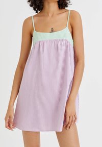 Robe à bretelles avec un haut vert clair et un bas rayé lilas et blanc. Fabriquée en tissu léger, elle présente une coupe ample et des bretelles spaghetti.