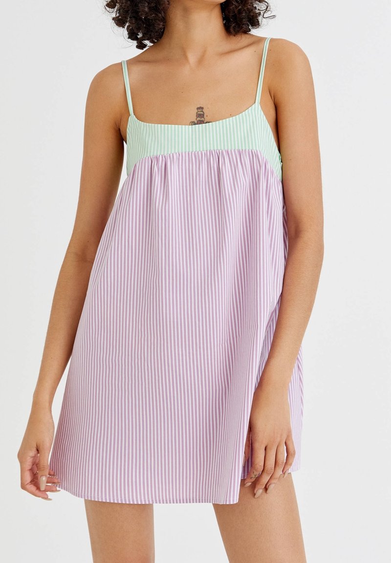 Robe à bretelles avec un haut vert clair et un bas rayé lilas et blanc. Fabriquée en tissu léger, elle présente une coupe ample et des bretelles spaghetti.