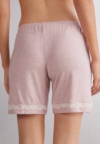 Lichtroze shorts van zachte stof, met een elastische tailleband en decoratieve witte kant aan de zoom. Gladde textuur, casual ontwerp.