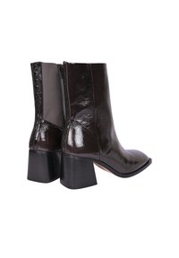 Bottes de cheville en cuir verni marron avec un bout pointu et un talon bloc. Fermeture éclair sur le côté avec un panneau mat contrastant. Texture lisse et design épuré.