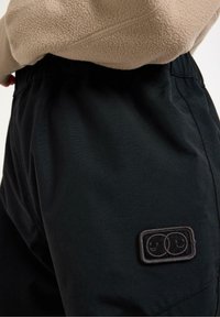 Svarta shorts med elastisk midja, sidfickor och en sydd logotypapplikation med två stiliserade ansikten på vänster sida.