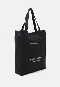 Black fabric tote bag with two long handles, featuring a front zip pocket and white text branding. Simple, rectangular design with matte texture.