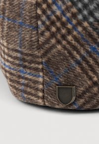 Pruunist ruudulisest villakapis, millel on sinised aktsendid ja tekstureeritud viimistlus. Külgedel on väike pronksist kilbi kujul logo.