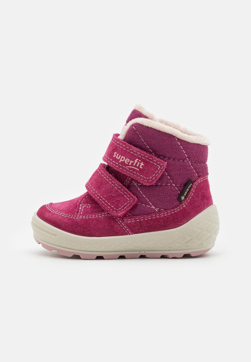 Roze suède enkellaars met twee klittenbandstraps, zachte witte voering, gestructureerde zool en diamantpatroonaccenten aan de zijkanten.