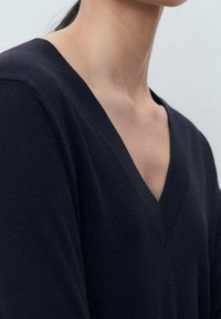 Granatowy sweter z dzianiny z głębokim dekoltem w kształcie litery V, cechujący się miękką fakturą i prostym wzornictwem. Brak widocznych wzorów lub elementów metalowych.