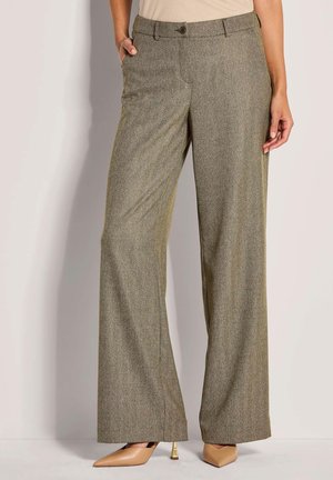 Vrouw in hooggerande, wijde bruine herringbone broek met een knoop en rits, gecombineerd met beige spitse hakken.