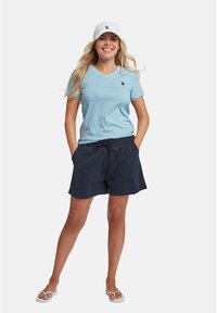Svijetloplava V-neck majica, tamnoplave kratke hlače s vezicom, bijela kapa s logotipom i bijele japanke. Ležerna ljetna odjeća.