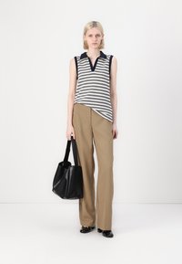 Gestreept mouwloos topje met een v-hals, gecombineerd met hoog-waist beige broeken. Model houdt een zwarte leren handtas vast; de setting is minimalistisch.