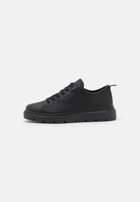 Black sneaker with a textured leather upper, round toe, and flat rubber sole featuring a jagged edge. Laces and short heel tab included.
