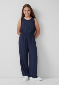 Navyblauer ärmelloser Jumpsuit mit elastischem Bund und weitem Bein, aus leichtem Stoff gefertigt. Kombiniert mit weißen Sneakern.