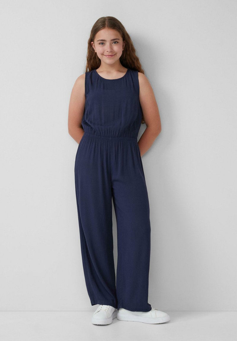 Navyblauer ärmelloser Jumpsuit mit elastischem Bund und weitem Bein, aus leichtem Stoff gefertigt. Kombiniert mit weißen Sneakern.