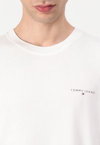 Witte katoenen T-shirt met een ronde hals. Bevat een klein "TOMMY JEANS" logo in het zwart op de borst en heeft een stoftextuur die zacht aanvoelt.