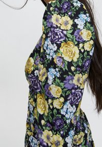 Abito floreale con una base nera decorata da fiori gialli, viola e blu. Maniche lunghe e silouette aderente. Tessuto dalla trama liscia.