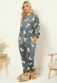 Veluuri loungewear-setti sinisessä, jossa on nallekarhuprintti. Sisältää pitkät hihat ja yhteensopivat housut, jotka on yhdistetty karvasiin nallekarhun tossuihin.
