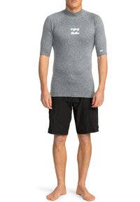 Rash guard gris de manga corta con un logo de color claro, combinado con shorts de baño negros. Textura suave, diseño ajustado para actividades acuáticas.
