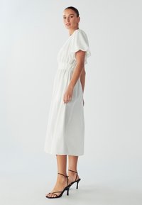 Biała midi sukienka z bufiastymi rękawami, elastycznym pasem i gładkiego materiału. W połączeniu z czarnymi sandałami na obcasie z cienkimi paskami i szpiczastym noskiem.