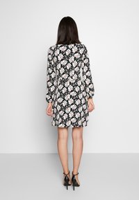 Blommig klänning med svart bakgrund, har långa ärmar, en figurnära midja och vita blommor med rosa inslag. Bärs med svarta klackar.