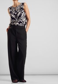 Ärmlös blus med ett svart och vitt blommönster, kombinerad med högmidjade svarta vida byxor och öppna skor med textur.