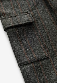 Grauer Stoff mit strukturierter Webart, der kontrastierende orange Streifen und ein gefaltetes Bündchen-Detail aufweist. Einfaches, funktionales Design.