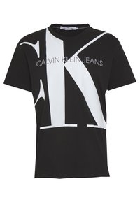 Musta lyhythihainen T-paita, jossa on ylikokoiset valkoiset "CK"-kirjaimet ja "Calvin Klein Jeans" -teksti tulostettuna rinnan kohdalla.